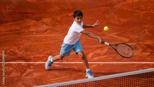 Young Indian boy playing tennis hitting backhand shot on clay court during training match action
