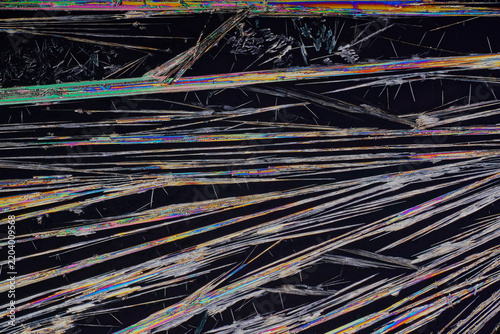 Polarized light microscopy of homegrown chemical crystals showing horizontal sharp needle structures and divergent crystal vectors on pitch black background for chemistry science abstract