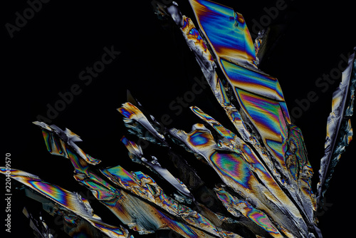 Abstract polarized light microscopy background of sharp crystalline prisms, 5x objective magnification, vibrant rainbow birefringence texture and mineral geology geometry on black