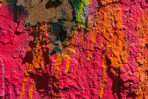 Abstract background on an old concrete wall. Multilayered bright pink paint with deep cracks and textured yellow drips. Grunge texture, peeling surface, and architectural relief