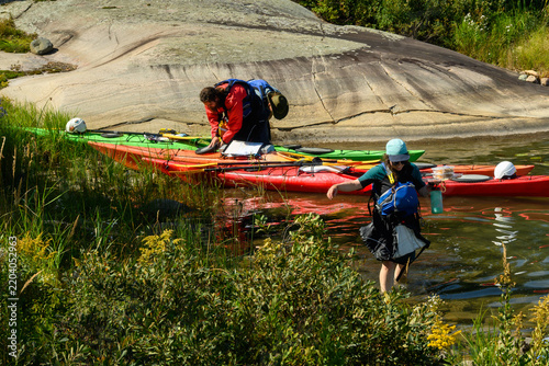 Quadro su tela Sea kayakers land at granite shore for lunch as one wades ashore carrying food o