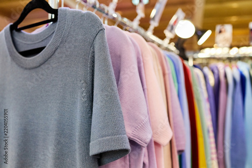 Soft pastel knit sweaters in gray, pink and various colors hanging on clothing rack in modern boutique store with warm lighting and bokeh background.