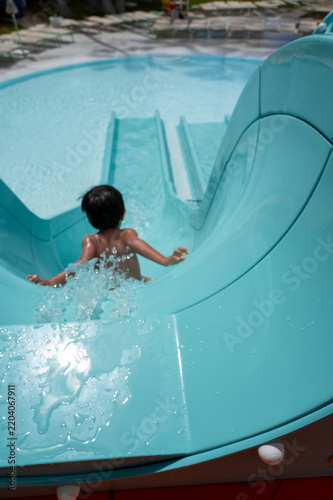 Fotografie Child slides down a turquoise water slide, arms spread, into splashing water