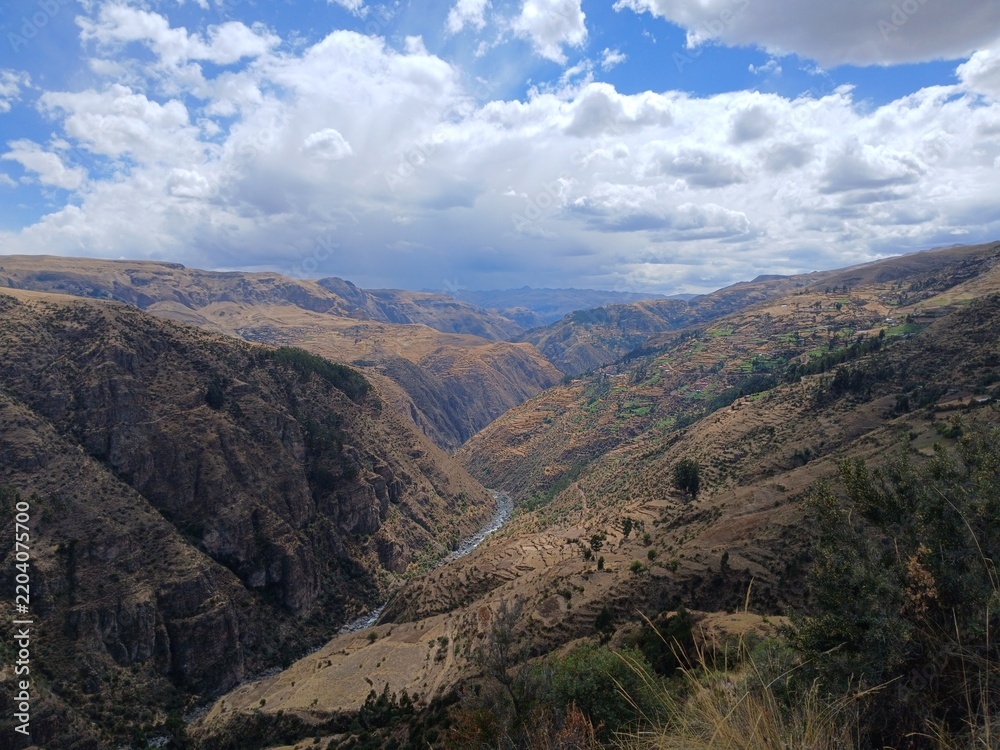 Obraz premium Valley with a distant river, mountains, forest, and a cloudy sky in the background in Surimana, Cusco, Peru.
