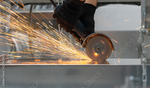 a worker in protective gloves cutting a metal with an angle grinder