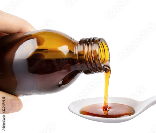 Amber medicinal syrup is being poured from a glass bottle in a white spoon isolated on white
