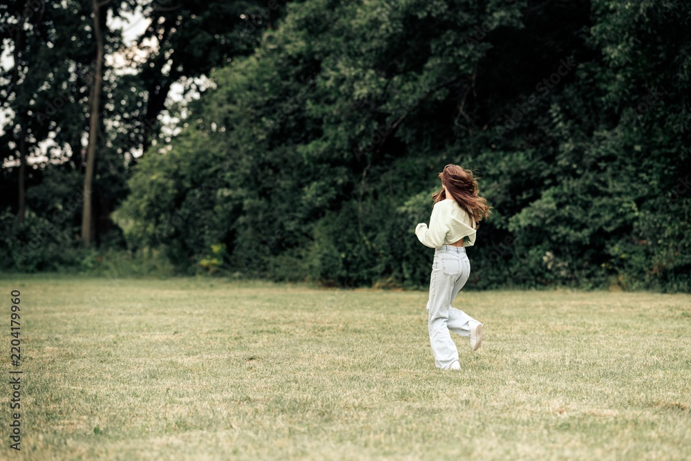 Obraz premium Young woman running across a grassy park field in casual outfit enjoying nature and freedom on a breezy day