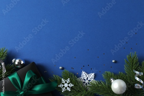 Top view of gift box with green bow and Christmas decorations on blue background, space for text