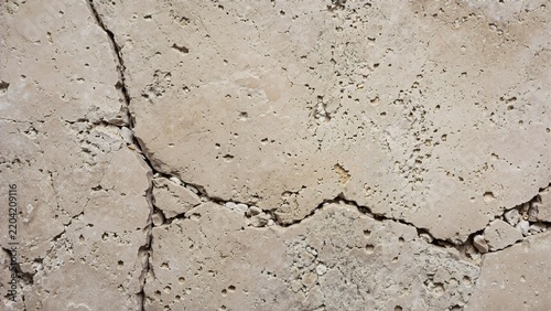 Cracked travertine stone tile with natural fissures and holes. Weathered beige limestone slab texture for architecture and masonry