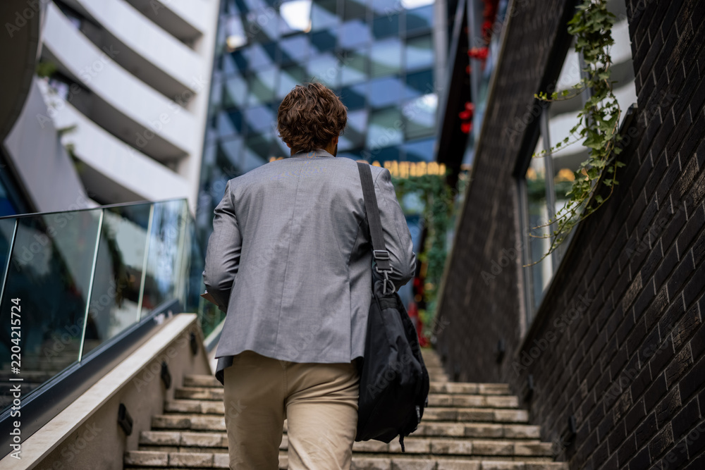 Obraz premium Rear view close up of young businessman carrying shoulder bag walking up stairs