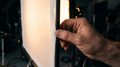 Close up view of a videographer or photographer hand adjusting and assembling professional studio lighting equipment diffusion fabric softbox panel modifier gear setup during production shoot session