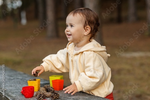 Toddler laughing joyfully while playing with pinecones outdoorssmil