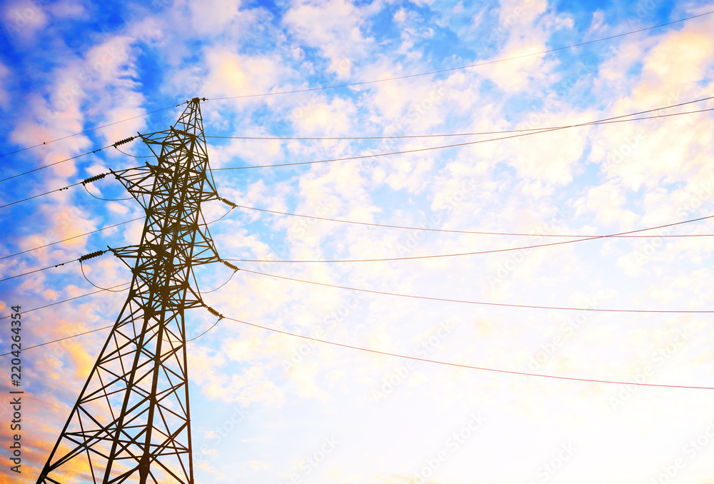 Obraz premium Silhouette of electricity pylon against blue sky with scattered clouds and warm golden hour lighting