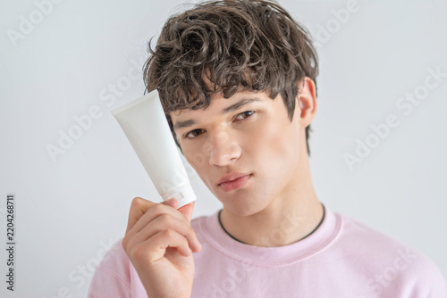 Foto Teenager holds cosmetic tube beside face with visible skin problems, breakout appearing exactly before important day, reality of growing up