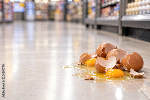 Broken eggs and yolks spill across a supermarket floor. Space for text.
