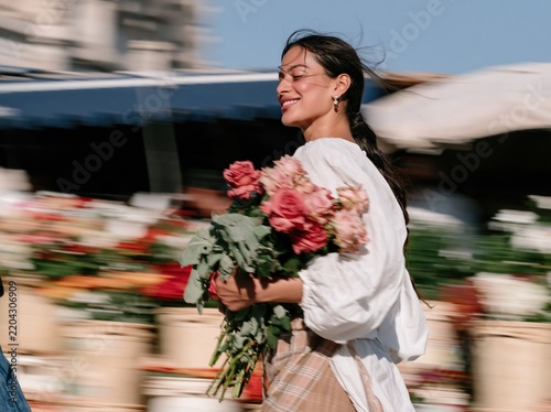 Pink roses bouquet held by a smiling Indian woman walking through a sunlit flower market, glowing and natural, for floral and lifestyle themes