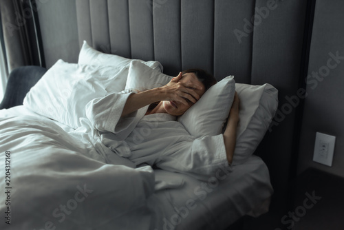 Exhausted woman waking up in bed covering her face with hand after a sleepless night