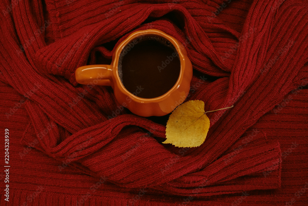 Obraz premium An orange mug of coffee resting on a red knitted sweater beside an open book and a yellow autumn leaf, with soft film grain, high quality photo