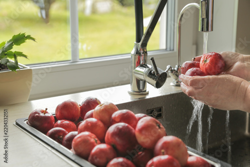 Washing fresh red apples under running water in home kitchen after autumn harvest
