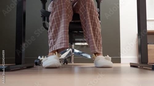 Person wearing plaid pajamas and plush reindeer slippers walks to office chair and sits down at desk. Concept of comfortable clothing and working from home