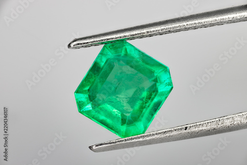 Colombian emerald cut green gemstone held in tweezers, close-up macro on white background 3