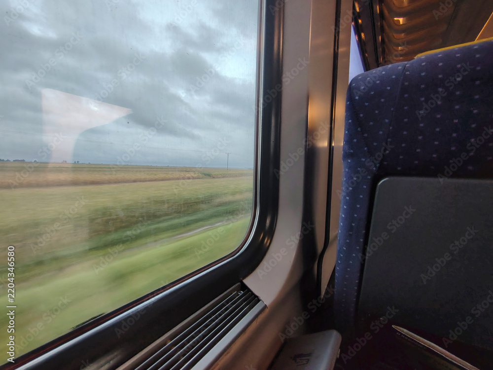 Obraz premium View from a train window of fields and countryside under a cloudy sky