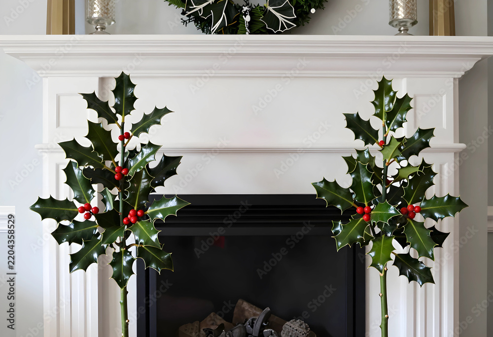 Naklejka premium Christmas home decor and holiday interior design, festive holly plants with red berries on a white fireplace mantel for seasonal winter celebration