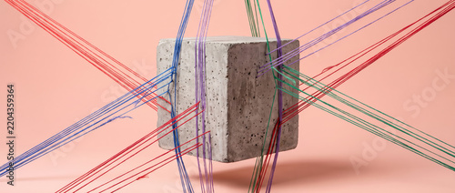 Concrete cube surrounded by colorful threads.