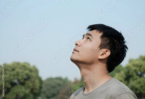 Hope and inspiration, young man looking up at the sky with optimistic expression and vision for the future in a peaceful outdoor park setting