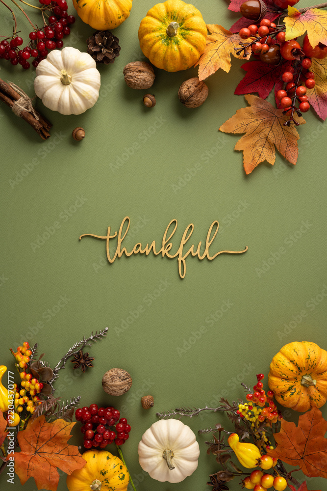Fototapeta premium Thankful autumn flat lay with pumpkins, leaves and Thanksgiving decorations on vertical pastel background with text Thankful