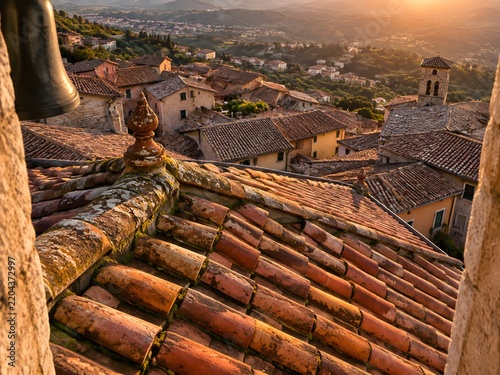 Curved terracotta pantiles running down a hillside town roofscape with moss in the joints and a weathered ridge