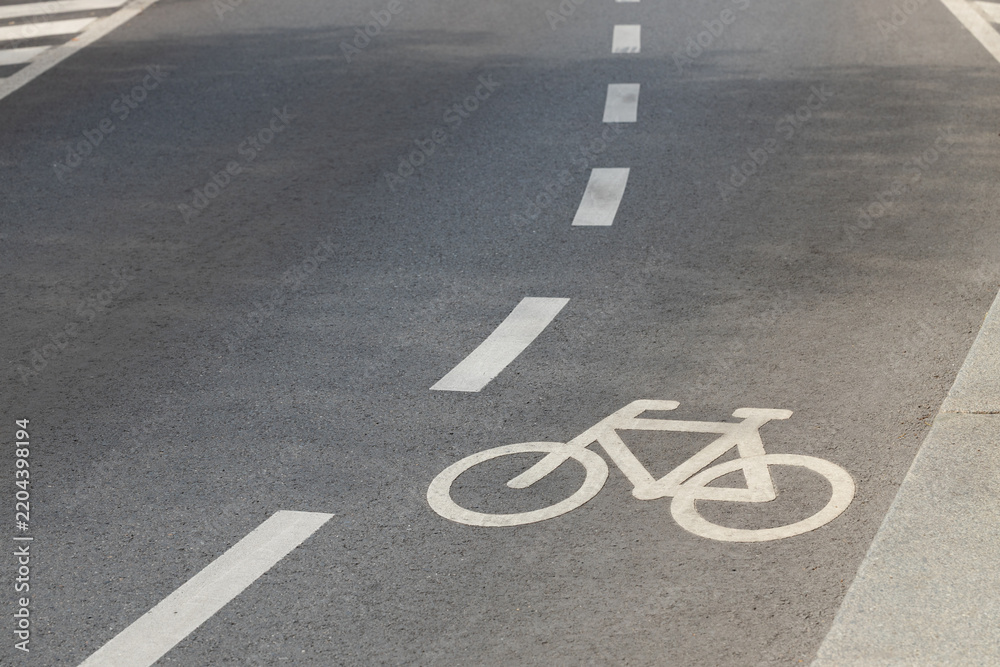 Obraz premium White bicycle lane symbol and dashed road markings on smooth asphalt beside concrete curb, viewed from above as urban transportation infrastructure in a dedicated cycling lane