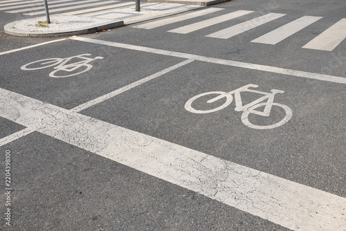 Bicycle lane markings and zebra crossing on urban asphalt street with painted cycling symbols, road lines, sidewalk island, and traffic infrastructure in city roadway