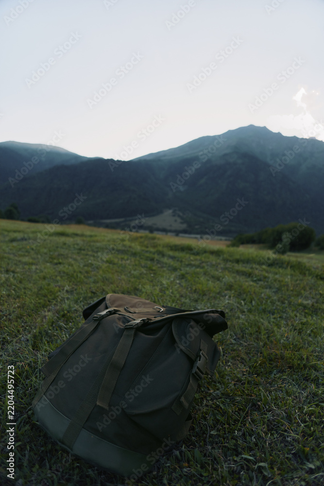 Fototapeta premium Backpack on a meadow with distant mountains, conveying outdoor travel, landscape, solitude, and a moment of quiet adventure in nature.