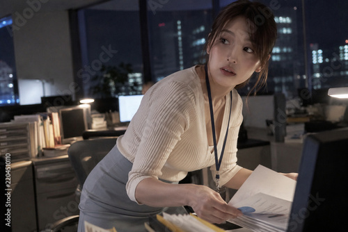 Naklejka 夜の机でグラフ入り資料を扱う白いカーディガンの女性