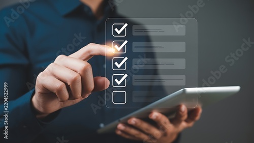 Man's finger checking off items on a digital checklist on a tablet with soft background lighting
