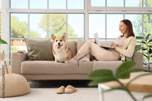Remote work and work-life balance, woman using laptop on sofa with her corgi ...