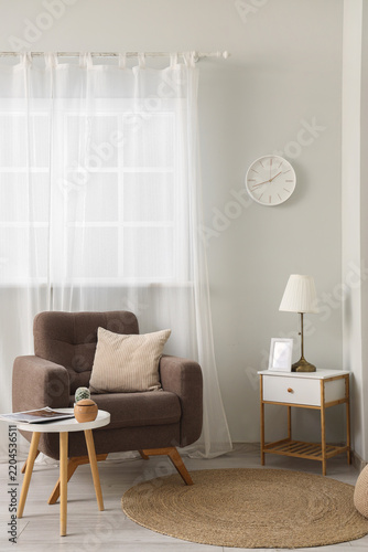 Interior of living room with wall clock, armchair and tables
