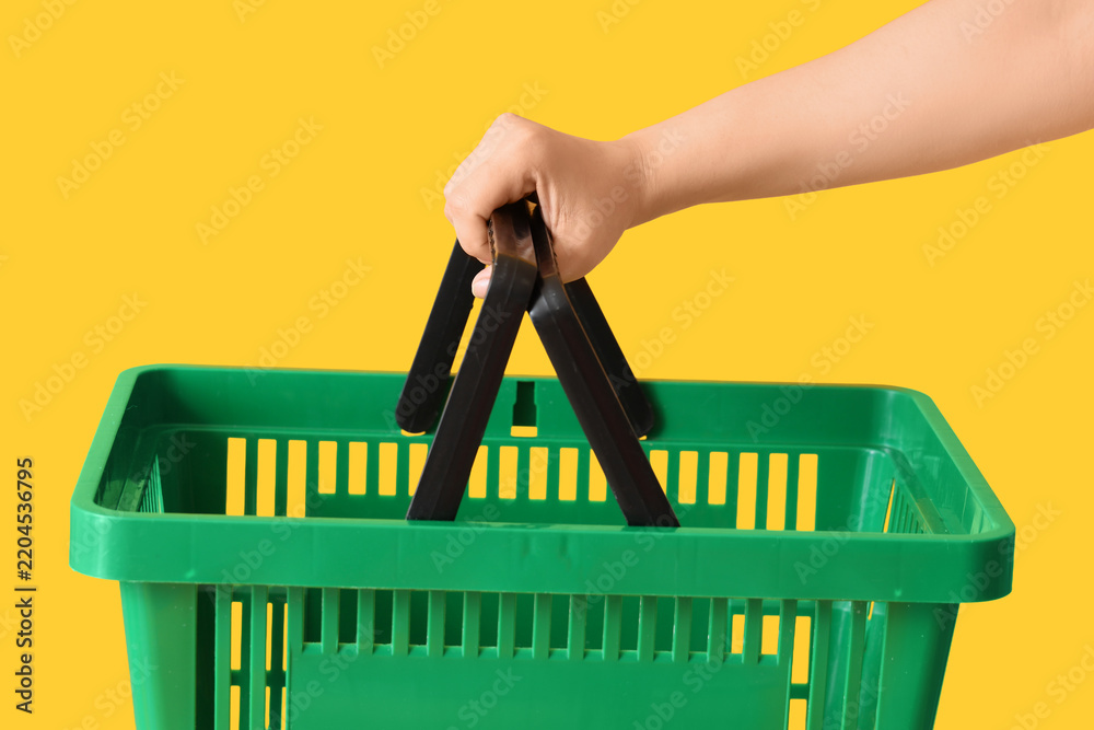 Obraz premium Female hand with green shopping basket on yellow background