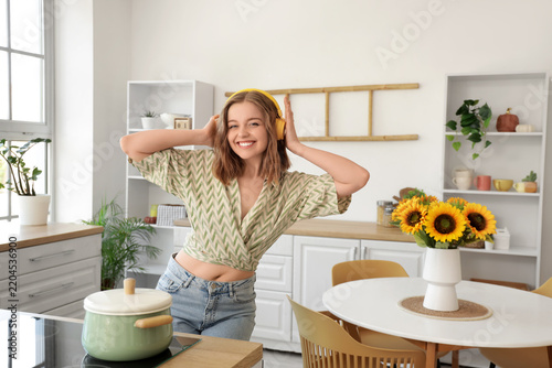 Cool young woman listening to music and dancing in kitchen