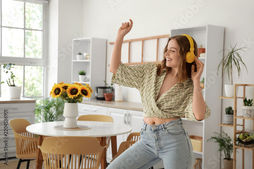 Cool young woman listening to music and dancing in kitchen