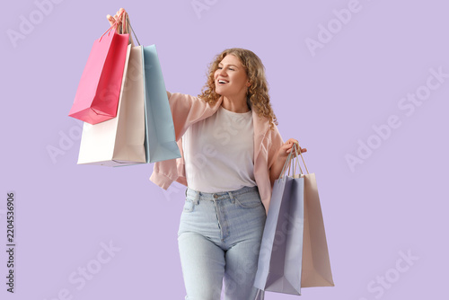 Beautiful young happy woman with shopping bags on purple background