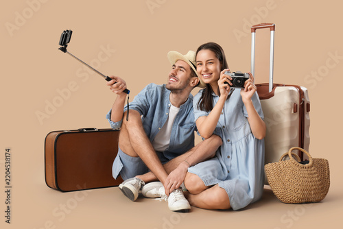 Beautiful young happy couple of tourists with suitcases and camera taking sel...