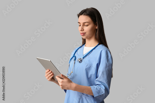 Young pretty female doctor with tablet on grey background
