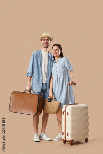 Beautiful young happy couple of tourists with suitcases on brown background