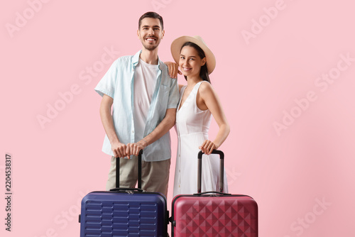 Beautiful young happy couple of tourists with suitcases on pink background