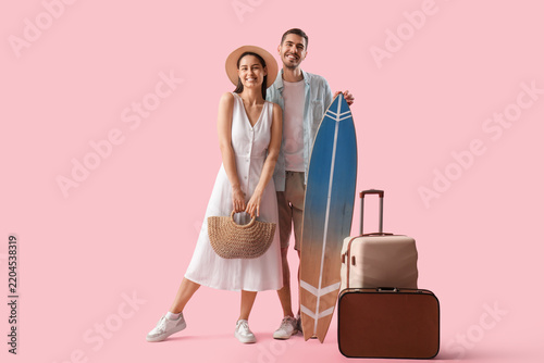 Beautiful young happy couple of tourists with suitcases and surfboard on pink...