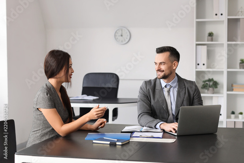 Human resources manager with laptop interviewing female applicant at table in...