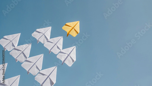 One yellow paper plane leading a formation of white paper planes on blue background with leadership innovation business strategy different teamwork creative motivation direction competition