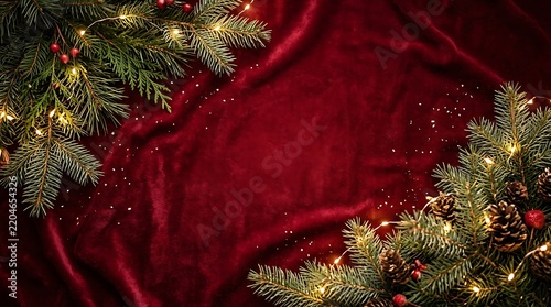 Festive christmas background with evergreen branches and glowing lights on red velvet fabric